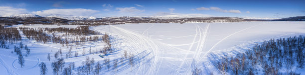 风景的空中全景从桦树森林到不同的方向上覆盖着白雪冰冻的山湖，Joesjo，瑞典拉普兰山脉的背景，阳光明媚的霜冻的一天雪地摩托步道图片下载