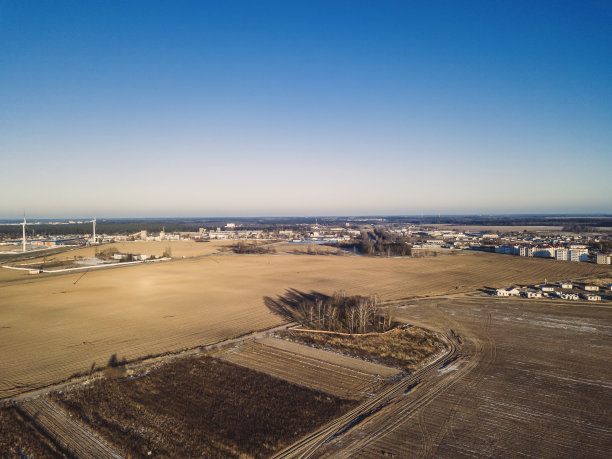 在一个阳光明媚、无雪的冬日，城市郊区的农田环绕着两座风力涡轮机。王座照片图片下载
