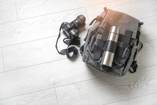 准备徒步旅行的冒险。踏青自然的概念。白色木地板上放着背包、热水瓶和相机。图片下载