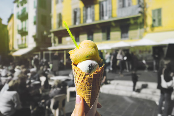 模糊的街道背景中，一个女人的手拿着意大利华夫蛋筒冰淇淋。图片下载