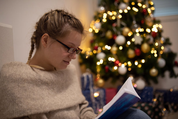 年轻女子在圣诞树旁看书图片下载