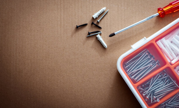 白橙色塑料盒中的塑料插头和螺钉的俯视图。螺丝刀，墙塞，和黑色螺丝棕色纸盒纹理。一套用于钻墙和安装的螺钉和塑料塞。图片下载