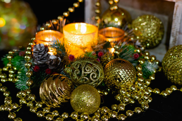圣诞装饰在黑色背景下的烛光。由金球和珠子组成，带有图案的镂空烛台和圣诞树的树枝。优雅的锥形和红色的浆果在节日里图片下载
