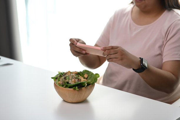 年轻超重女性用智能手机拍蔬菜沙拉照片。图片下载