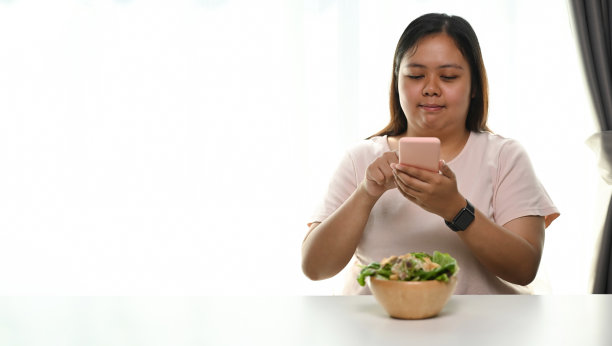 超重的年轻女子用智能手机拍蔬菜沙拉照片。图片下载