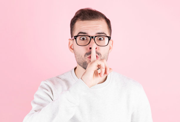 年轻英俊的男子在粉红色的背景要求安静与手指在嘴唇上。沉默与秘密的概念。图片下载