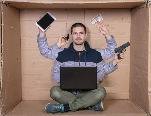 一个多任务的男人坐在一个狭小的纸板办公室里，在家工作图片下载