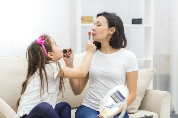 妈妈和小女儿微笑着拿着化妆刷的照片。图片下载