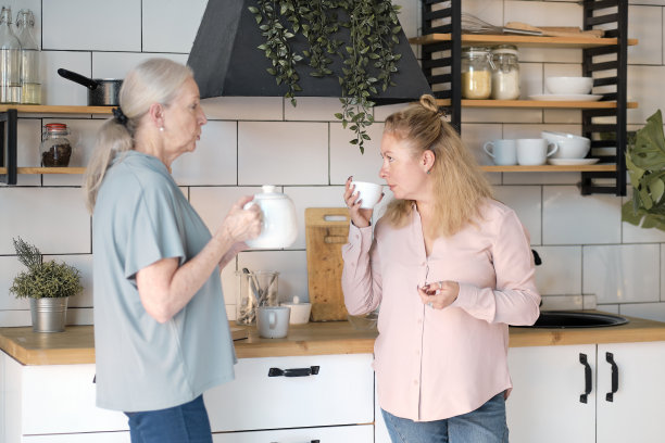 友好的家人在家里看照片。一位年长的女士正在和她的女儿叙旧。他们正在厨房里喝茶。在客厅有女性看护的老年妇女图片下载