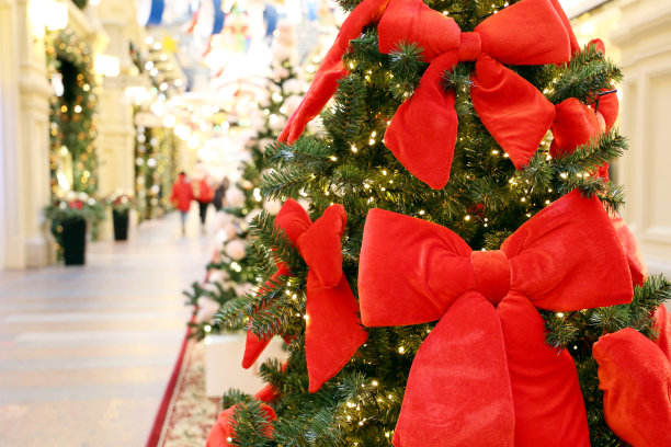 圣诞树用红色的节日蝴蝶结在购物中心的节日灯和行人的背景图片下载
