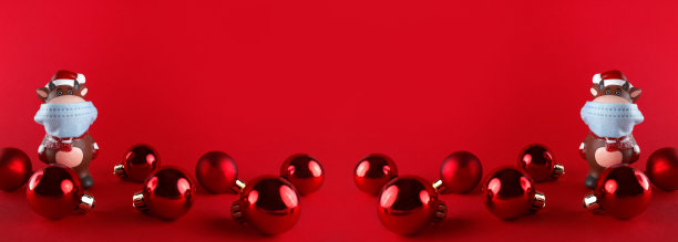 陶瓷雕像的牛在医疗面具和圣诞球在红色的背景。宽横幅与复制空间。2021年新年的象征。图片下载