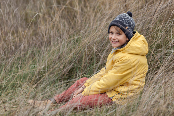 快乐的小男孩坐在高高的草地上。图片下载