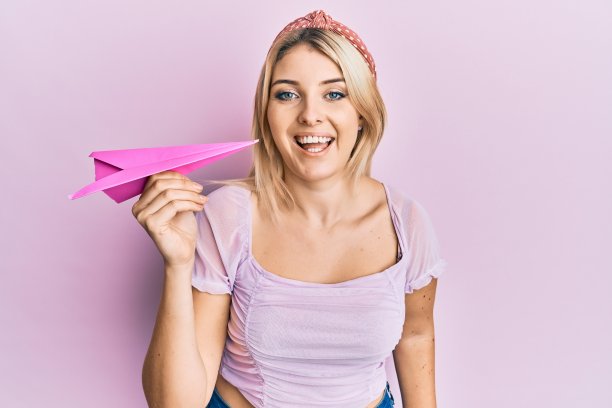 年轻的白人妇女拿着纸飞机笑得很大声，因为有趣的疯狂笑话。图片下载