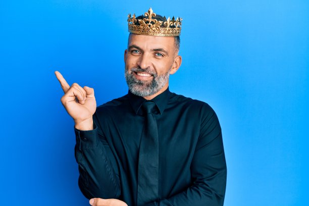 中年英俊的商人戴着国王皇冠微笑着幸福地指着手指的一边图片下载
