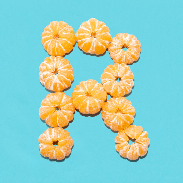 蓝色背景下去皮的橘子上的字母R的创意布局。Flatlay。图片下载