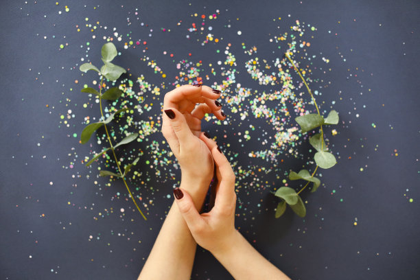 女性的手与指甲在桌子上与植物和五彩纸屑图片下载