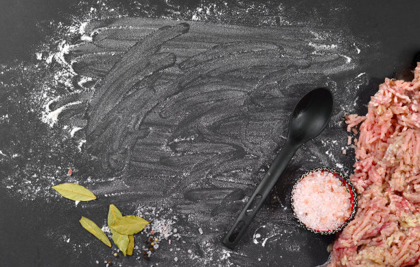 剁碎的猪肉和鸡肉放在撒有面粉的黑色桌子上。一碗盐，月桂叶和胡椒，一个黑勺。图片下载