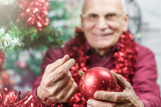 戴眼镜的老年男性市民在笔记本电脑屏幕上显示红色的圣诞树球图片下载
