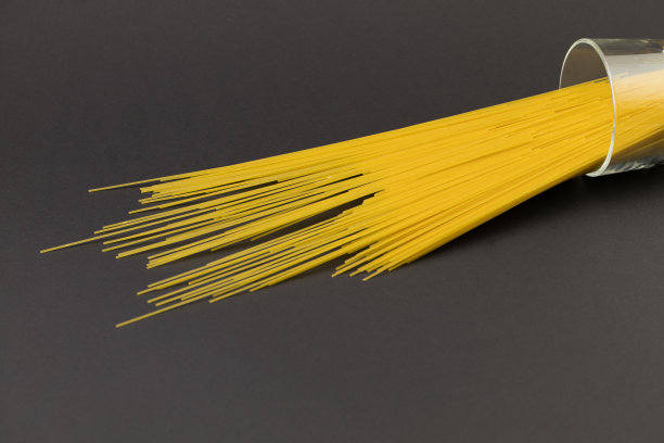 深色的背景上放着一个大杯子里的长通心粉图片下载