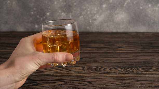 手里拿着一杯棕色朗姆酒。手持一杯波旁威士忌。一杯加冰的苏格兰威士忌图片下载