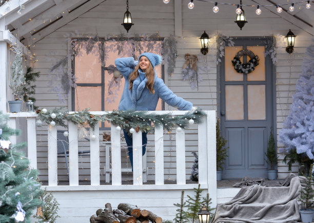 一个快乐的女孩戴着高帽子、皮大衣、手套站在圣诞屋的门廊上!新年快乐，圣诞快乐!图片下载