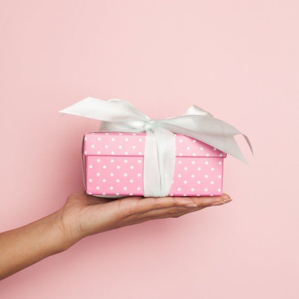 最小的背景组成手持粉红色礼物与白色丝绸缎带上柔和的粉红色背景图片下载