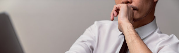 西装革履的严肃商人双手摸着下巴，看着办公室里的笔记本电脑。图片下载