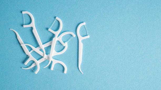 蓝色背景的牙线剔牙。软牙线。牙科挑选。带牙线的白色塑料牙签图片下载