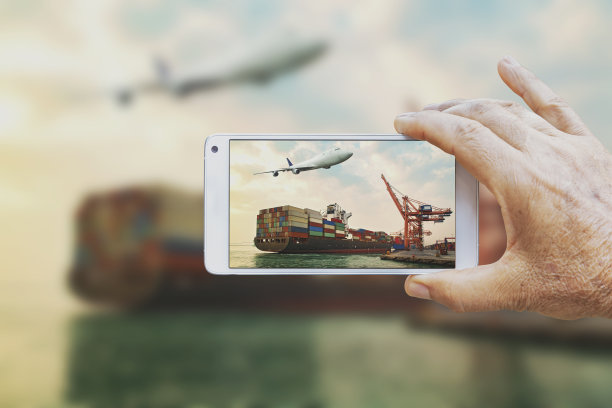 在一个商业港口，一名男子用智能手机拍下了集装箱装卸活动的照片。图片下载