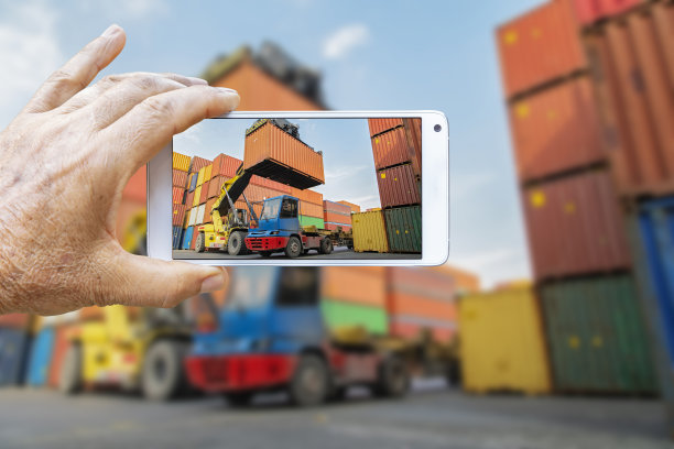 在一个商业港口，一名男子用智能手机拍下了集装箱装卸活动的照片。图片下载