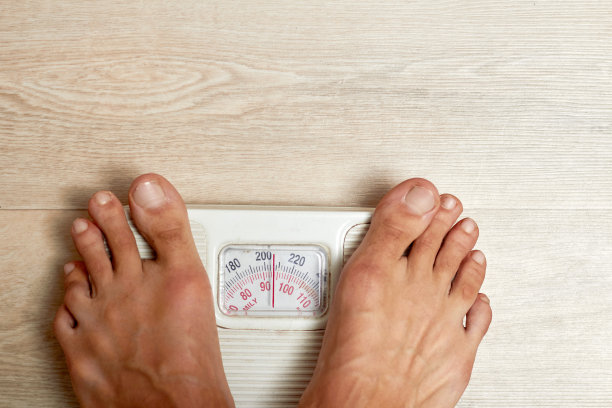 一个人光着脚站在秤上。照片显示了地板、鳞片和脚。图片下载