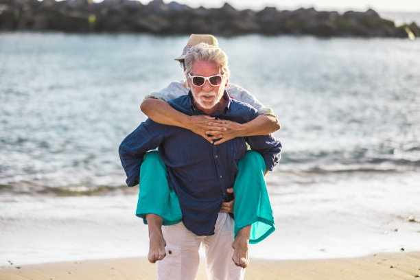 老年夫妻在暑假一起在海滩游玩——旅游成熟的男人和女人互相背着，享受海洋旅行图片下载