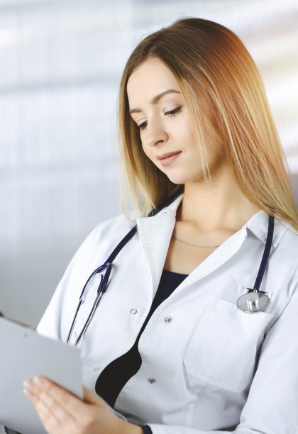 一位年轻乐观的女医生坐在诊所阳光橱柜的办公桌前，正在使用写字板。友好的女医生的肖像妇女与听诊器。医院里完美的医疗服务。医学的概念图片下载