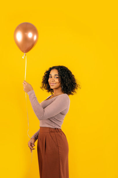 微笑的年轻女子拿着气球在黄色的背景图片下载