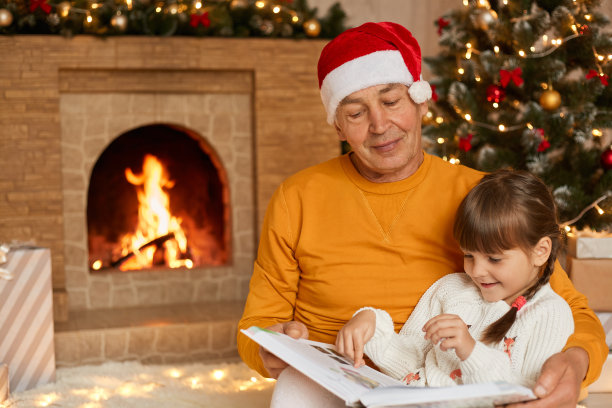 全家人集中坐在客厅的地板上，看童话故事，看照片，一起度过圣诞夜，戴着圣诞老人帽的老人，爷爷和孙女。图片下载