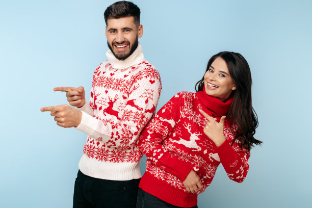 一对积极的夫妇穿着圣诞毛衣指着蓝色的背景。图片下载
