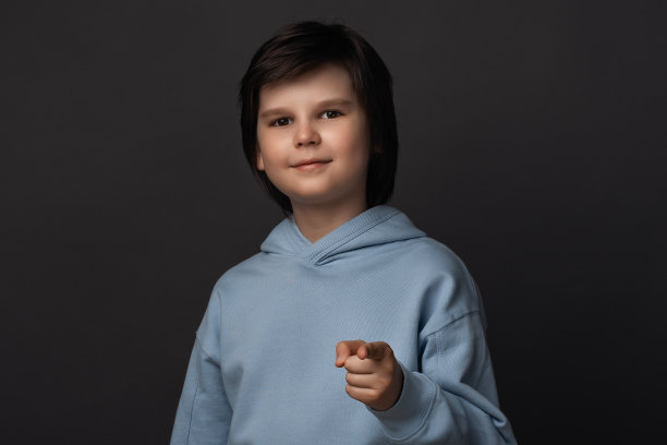 10-12岁的可爱男孩看着镜头，用手指着你。工作室拍摄，灰色背景图片下载