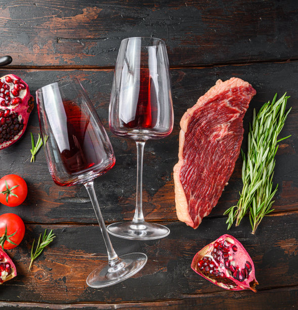两杯红酒靠近生牛排在旧的深色木制桌子上顶视图。大尺寸。图片下载