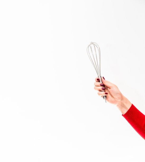 女人的手牢牢地握着做饭用的金属搅拌器。白色背景。图片下载