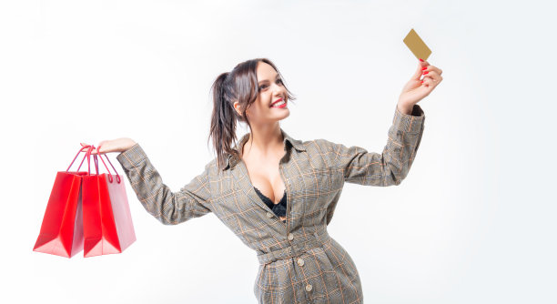 迷人的棕发女子在工作室里摆姿势，拿着红色包裹和银行卡，礼物概念，节日前购物，白色背景图片下载