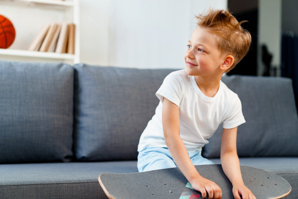 小男孩坐在家里的沙发上，拿着滑板图片下载