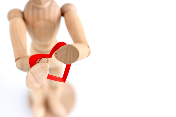 灰色背景下，木制模特手里拿着红纸做的心。时尚简约的情人节概念，爱，真实的感觉。副本的空间。图片下载