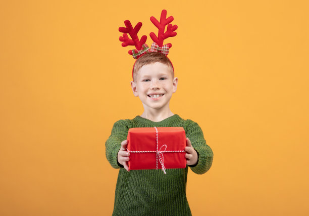 微笑的男孩在黄色背景上赠送圣诞礼物图片下载
