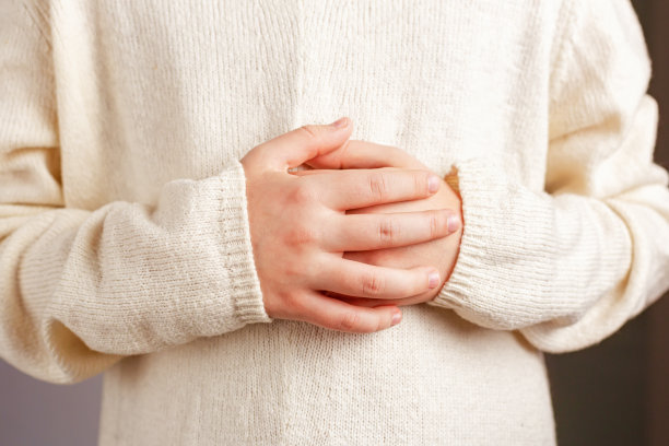 这是一个孩子的特写镜头，他穿着一件浅色的香槟色针织毛衣，双手交叉放在肚子上。图片下载