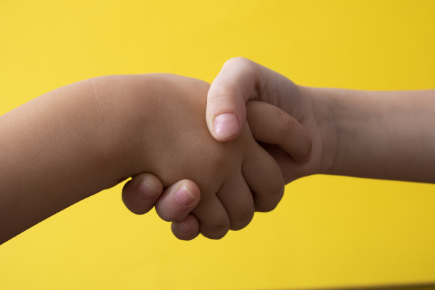 在黄色背景下握手。孩子们的手，靠近点图片下载