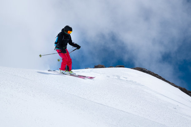 女子滑雪运动员在雪坡上的一个跳跃，背景是蓝色的天空的山和云。女子免费乘车和极限滑雪图片下载