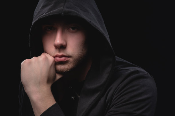 肖像的一个大的有吸引力的男子在一个黑色兜帽持有他的下巴与他的手在沉思的姿势。歹徒阴影下的神秘面孔图片下载
