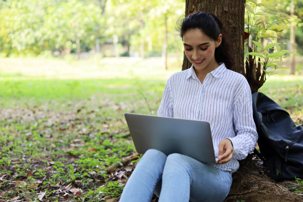 美丽的年轻女子工作和玩笔记本电脑在花园公园。图片下载