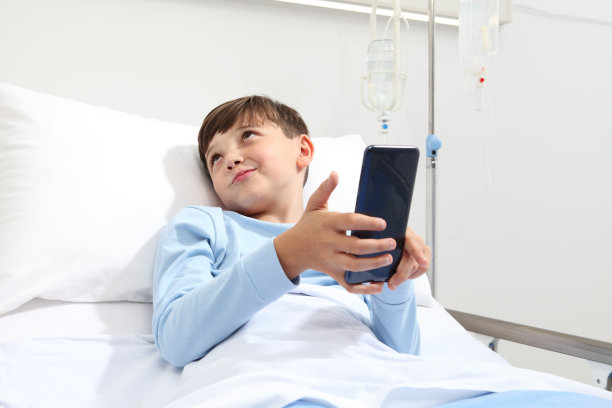 一个孩子独自躺在病床上看智能手机的照片图片下载