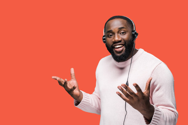 非裔美国呼叫中心工作人员戴着耳机，穿着休闲装，站在一个红色的孤立背景上，微笑着与客户交流图片下载